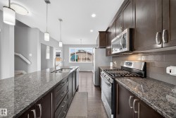 Kitchen featuring an expansive island with an undermount sink, granite-style countertops, dark wood cabinetry, stainless steel appliances, and wood-finish flooring - 