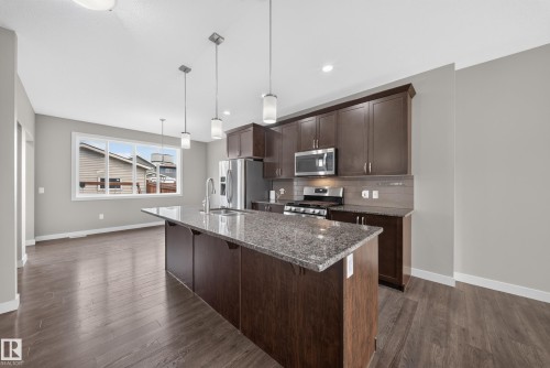 Kitchen featuring a large island with a stone countertop, dark wood-finish cabinetry, stainless steel appliances, and pendant lighting - 2331 Casey Crescent Sw, Edmonton, AB 
