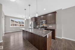 Kitchen featuring a large island with a stone countertop, dark wood-finish cabinetry, stainless steel appliances, and pendant lighting - 
