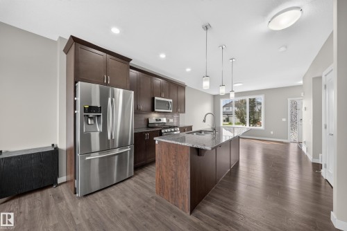 Kitchen featuring dark wood cabinetry, stainless steel appliances, granite countertops, and a central island with pendant lighting - 2331 Casey Crescent Sw, Edmonton, AB 