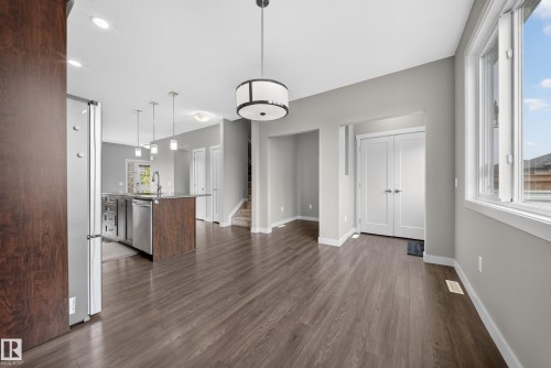 Open-concept living area featuring wood-finish flooring, a contemporary drum pendant light fixture, and a kitchen island with stainless steel appliances - 2331 Casey Crescent Sw, Edmonton, AB 
