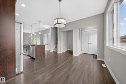 Open-concept living area featuring wood-finish flooring, a contemporary drum pendant light fixture, and a kitchen island with stainless steel appliances - 