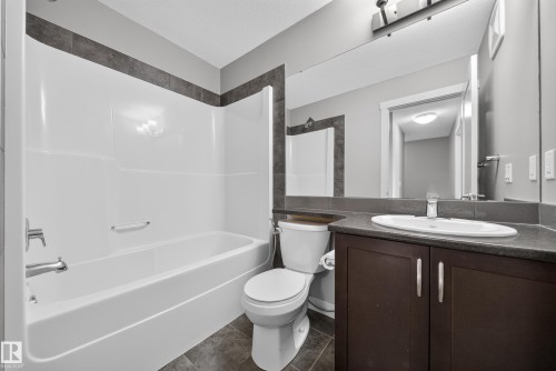 Bathroom featuring a white tub/shower combination with chrome fixtures, a dark wood-finish vanity with a built-in sink, a large mirror, and gray tile flooring - 2331 Casey Crescent Sw, Edmonton, AB 