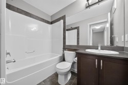 Bathroom featuring a white tub/shower combination with chrome fixtures, a dark wood-finish vanity with a built-in sink, a large mirror, and gray tile flooring - 