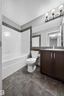 Full bathroom featuring a white tub/shower combination with dark accent tiling - 