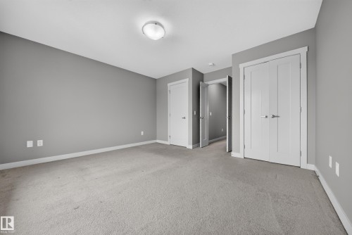 Carpeted room with a flush-mount ceiling light fixture, neutral gray wall paint, white baseboards, and multiple white panel doors - 2331 Casey Crescent Sw, Edmonton, AB 