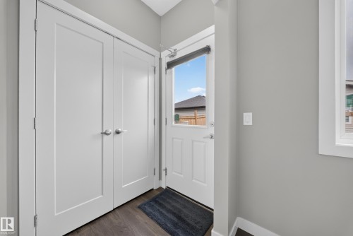 Entryway featuring a solid panel front door with frosted glass, wood-finish flooring, and a pair of white bifold doors with brushed nickel hardware - 2331 Casey Crescent Sw, Edmonton, AB 