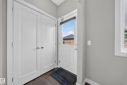 Entryway featuring a solid panel front door with frosted glass, wood-finish flooring, and a pair of white bifold doors with brushed nickel hardware - 