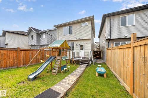 Fenced backyard featuring a wood deck, a wooden play structure with a slide and swings, and a grass lawn - 2331 Casey Crescent Sw, Edmonton, AB 