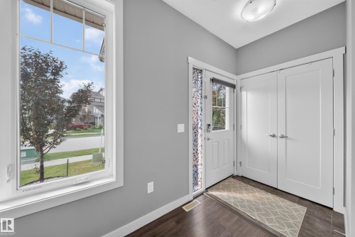 Entryway featuring wood-finish flooring, a white paneled entry door with a clear glass insert, and double bi-fold closet doors with brushed nickel hardware - 2331 Casey Crescent Sw, Edmonton, AB 