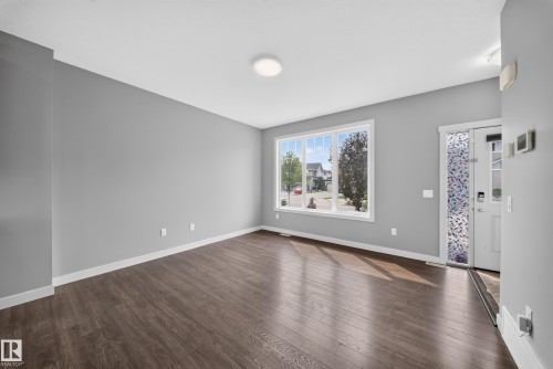 Open concept living space featuring wood-finish flooring, a large picture window, and neutral gray walls - 2331 Casey Crescent Sw, Edmonton, AB 