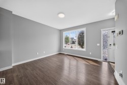 Open concept living space featuring wood-finish flooring, a large picture window, and neutral gray walls - 