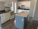 Kitchen featuring white cabinetry, dark stone countertops, a light-colored island with a solid surface countertop, wood-finish flooring, and a white tile backsplash - 15922 92 Avenue, Edmonton, AB 