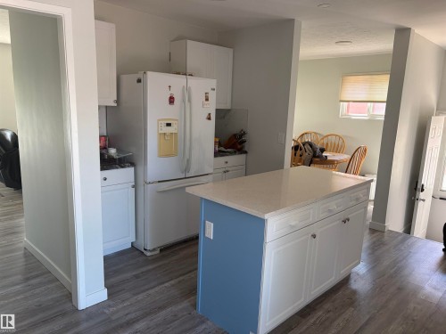 Kitchen featuring a central island with a blue base and white cabinetry, a light-toned countertop, and wood-finish flooring - 15922 92 Avenue, Edmonton, AB 