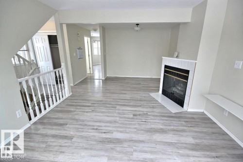 Spacious interior featuring wood-finish flooring, a white tiled fireplace surround, and a white staircase with balusters - 9457 156 Street, Edmonton, AB 
