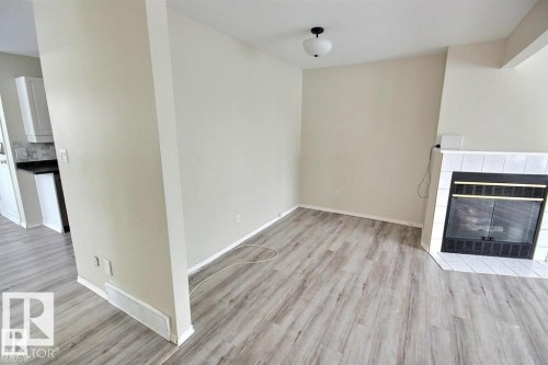 Living area featuring light wood-finish flooring, neutral wall tones, a white tile fireplace with a black iron insert, and a ceiling-mounted light fixture - 9457 156 Street, Edmonton, AB 