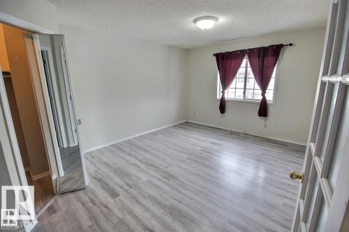 Spacious room featuring light wood-finish flooring, a window with security bars, and a ceiling-mounted light fixture - 9457 156 Street, Edmonton, AB 