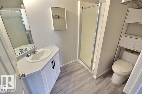 Bathroom featuring a vanity with an integrated sink, a shower enclosure with a clear glass panel, a toilet, and built-in shelving with cabinet storage - 9457 156 Street, Edmonton, AB 