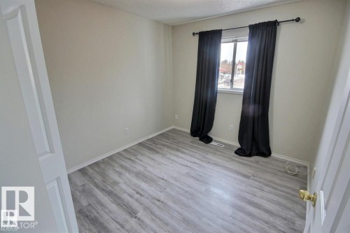 Room featuring light gray walls, wood-finish flooring, a window with black curtains, and white baseboards - 9457 156 Street, Edmonton, AB 