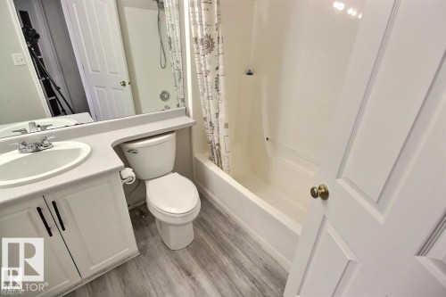 Bathroom featuring a single vanity with an integrated sink, a white toilet, and a white bathtub with a shower - 9457 156 Street, Edmonton, AB 