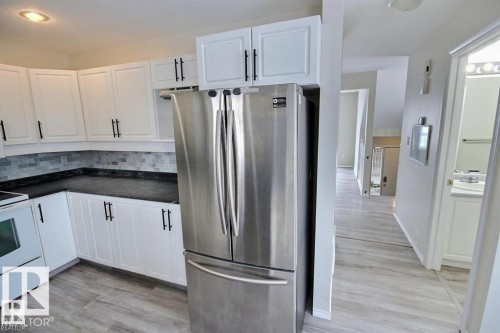 Kitchen featuring white shaker-style cabinetry with black hardware, dark countertops, and a gray subway tile backsplash - 9457 156 Street, Edmonton, AB 