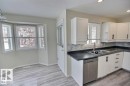 Kitchen featuring light wood-finish flooring, white cabinetry with black hardware, a stainless steel dishwasher, a dual basin sink with a gooseneck faucet, and a stone-look countertop with a tile backsplash - 9457 156 Street, Edmonton, AB 