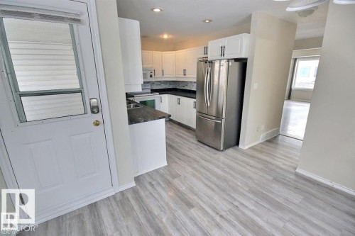 Kitchen featuring wood-finish flooring, white cabinetry, dark countertops, and stainless steel appliances - 9457 156 Street, Edmonton, AB 