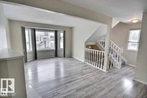 Spacious living area featuring bay windows, light wood-finish flooring, and a white baluster staircase - 9457 156 Street, Edmonton, AB 