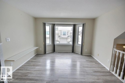 Bright living space featuring a bay window, light wood-finish flooring, a built-in wall shelf, a white painted staircase, and neutral wall tones - 9457 156 Street, Edmonton, AB 