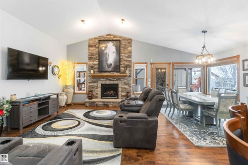 The spacious living area features vaulted ceilings, hardwood floors, a stone fireplace, and large windows providing natural light - 61 Linkside Blvd, Spruce Grove, AB 