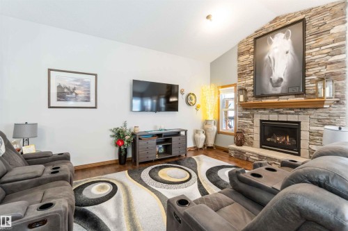 Spacious living area featuring a stone fireplace with a wooden mantle, hardwood floors, and a vaulted ceiling - 61 Linkside Blvd, Spruce Grove, AB 