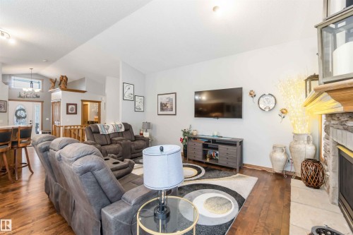 Living room with hardwood floors, a stone fireplace, and a vaulted ceiling - 61 Linkside Blvd, Spruce Grove, AB 