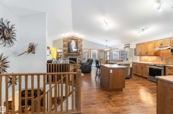 Open-concept living space featuring hardwood floors, a kitchen with wooden cabinetry and stainless steel appliances, and a living area with a stone-clad fireplace - 
