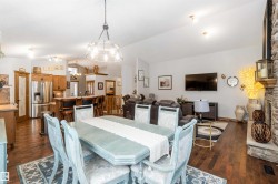 The open concept living area features hardwood floors throughout, a dining area with a chandelier, and a living room with a stone fireplace - 