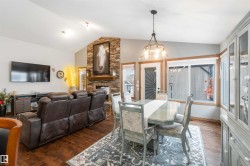 Open-concept living and dining area featuring hardwood floors, a vaulted ceiling, and a stone-faced fireplace - 