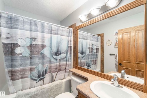 Bathroom featuring a vanity with an oval sink, a mirror with a wooden frame, and a bathtub with a shower curtain - 61 Linkside Blvd, Spruce Grove, AB 