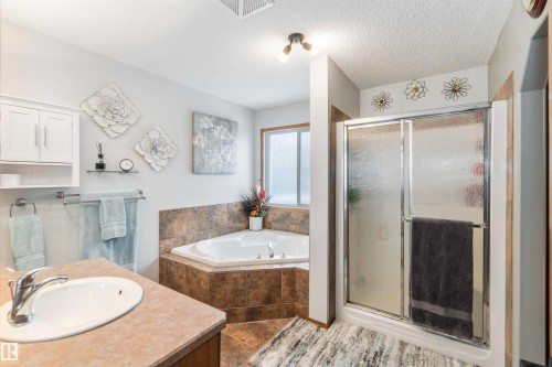 Well-appointed bathroom featuring a corner bathtub, a stand-up shower with a glass door, a vanity with an integrated sink, and tiled flooring - 61 Linkside Blvd, Spruce Grove, AB 