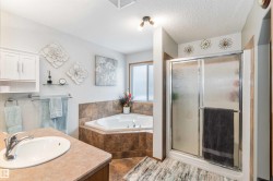 Well-appointed bathroom featuring a corner bathtub, a stand-up shower with a glass door, a vanity with an integrated sink, and tiled flooring - 