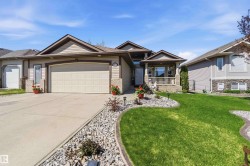 Contemporary home with an attached garage, featuring a covered porch with white railing, and a landscaped front yard with rock beds and manicured lawn - 
