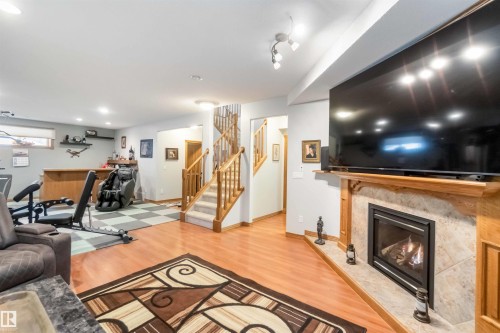 The property features a versatile lower level with wood-look flooring, a fireplace with a stone surround, and a staircase with wood railings and carpeted treads - 61 Linkside Blvd, Spruce Grove, AB 
