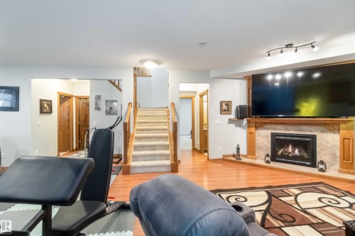 This spacious living area features hardwood flooring, a fireplace with a tiled surround and wood mantel, and a carpeted staircase with wood railings - 61 Linkside Blvd, Spruce Grove, AB 