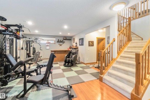 The property features a staircase with carpeted treads and wooden railings, alongside a versatile area with checkered floor tiles - 61 Linkside Blvd, Spruce Grove, AB 
