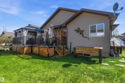 Expansive backyard featuring a manicured lawn, a raised wooden planter, and a multi-tiered wooden deck with black metal railings - 