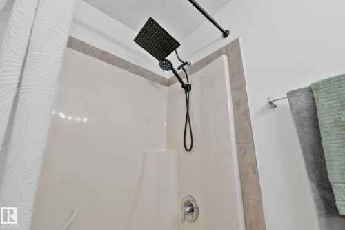 Shower stall featuring a black rain shower head with an attached handheld sprayer, chrome fixtures, and a tiled border - 5161 54 Avenue, Redwater, AB - Indoor Photo Showing Bathroom