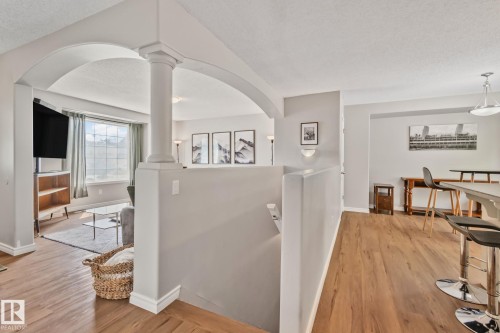 Open-concept living area featuring an arched entryway with a decorative column, wood-finish flooring, and a large window with white trim - 5161 54 Avenue, Redwater, AB - Indoor Photo Showing Other Room