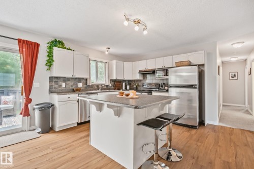 Kitchen featuring an island with seating, stainless steel appliances, wood-finish flooring, white cabinetry, and sliding glass door access to an outdoor area - 5161 54 Avenue, Redwater, AB - Indoor Photo Showing Kitchen