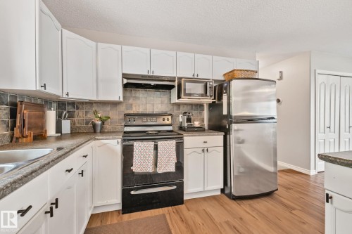 Kitchen featuring white cabinetry, a dark tile backsplash, dark countertops, a black electric range, and wood-finish flooring - 5161 54 Avenue, Redwater, AB - Indoor Photo Showing Kitchen