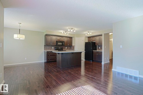 Open-concept kitchen and dining area featuring rich wood-finish flooring, dark cabinetry, a central island with a light-toned countertop, and recessed lighting - 6215 60 Street, Beaumont, AB - Indoor Photo Showing Kitchen