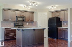 Open-concept kitchen featuring dark wood cabinetry, granite countertops, tile backsplash, a central island, and black appliances - 
