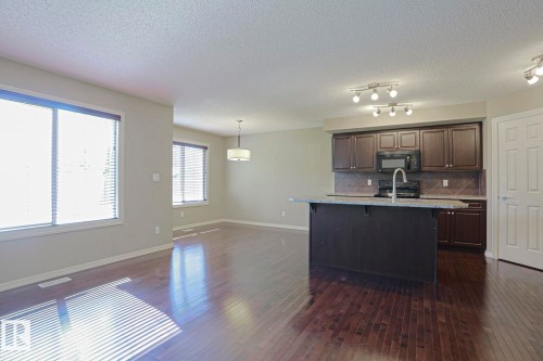 Kitchen featuring dark wood cabinetry, a central island with a light-toned countertop, and stainless steel appliances - 6215 60 Street, Beaumont, AB - Indoor Photo Showing Kitchen